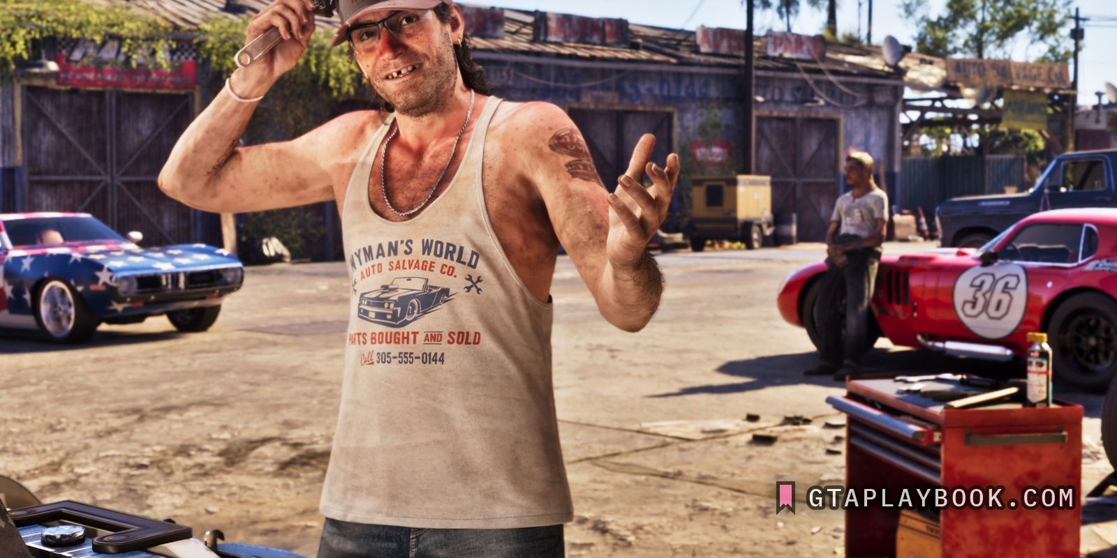 A man in a Wyman's World Auto Salvage Co. shirt on a yard of project cars, with the phone number on his chest